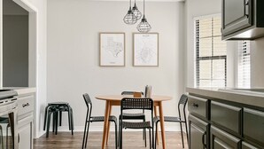 Una cuina moderna amb sòl de fusta, una taula de dinar amb cadires i dos mapes emmarcades a la paret.