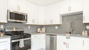 A modern kitchen with white cabinets, stainless steel appliances, and a grey backsplash. - You Had Me at Merlot-Pet Friendly 30 Day (Temecula)