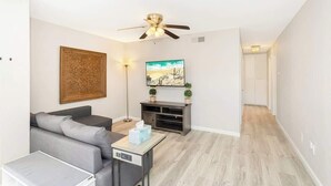 A modern living room with a grey sofa, a coffee table, a TV, a ceiling fan, and a painting on the wall. - You Had Me at Merlot-Pet Friendly 30 Day (Temecula)