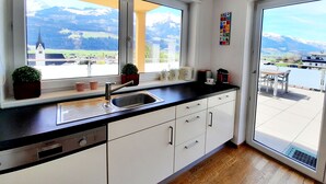 A kitchen with a view of mountains, a dining area with a table and chairs, and a window with a view of a church. - Piesendorf Pad Stunning Views Sleeps 8 (Piesendorf)