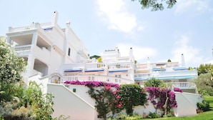 Un edificio blanco con varios balcones y un jardín lleno de flores rosadas.