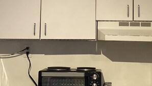 Keittiössä on valkoiset kaapit, mikroaaltouuni ja puinen koriste-esine työtasolla.