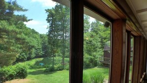 A view from a room with large windows overlooking a well-maintained garden with a lawn, trees, and a small pond.