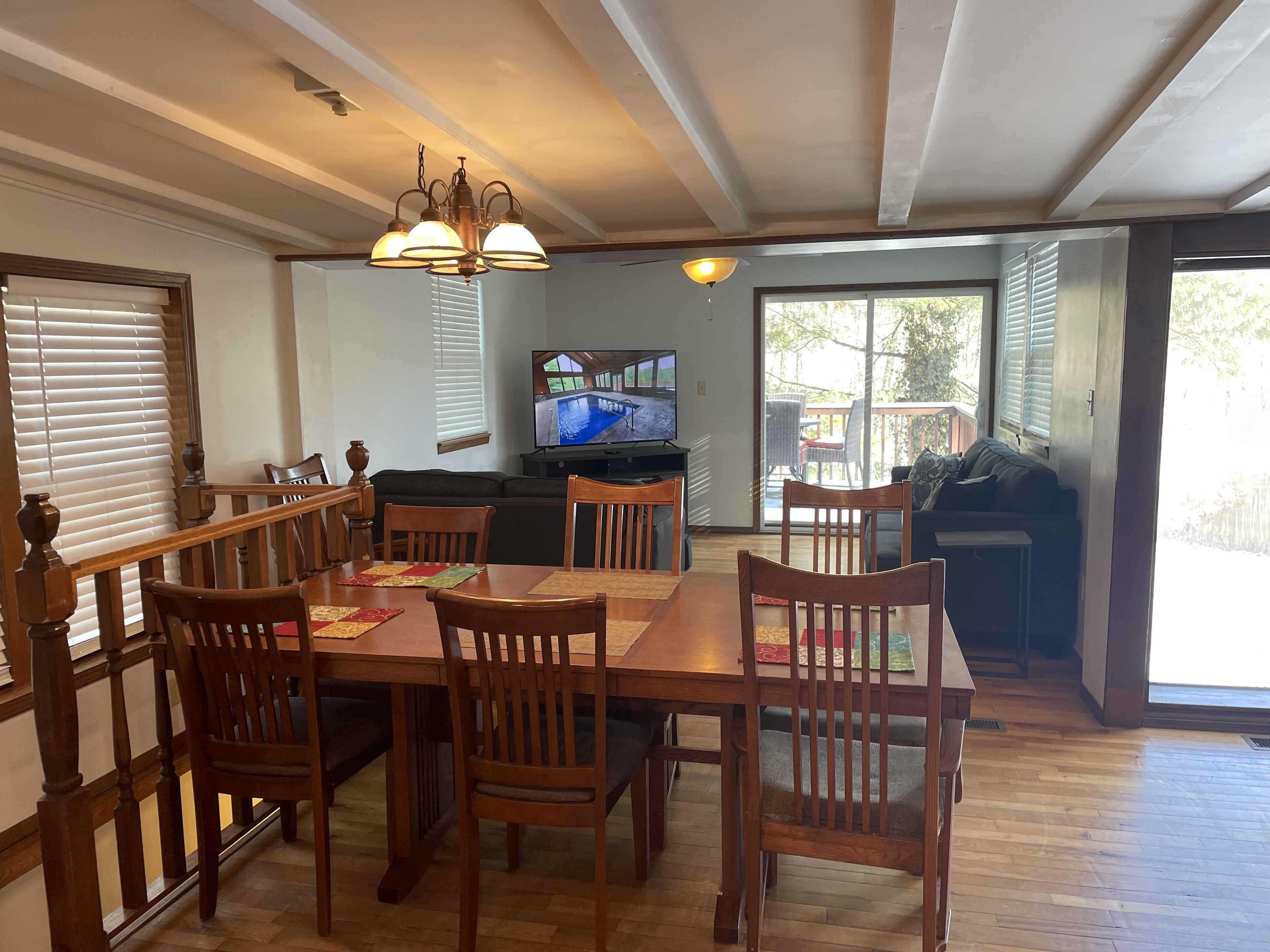 A dining area with a wooden table and chairs, a television, and a view of the outdoors.
