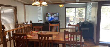 A dining area with a wooden table and chairs, a television, and a view of the outdoors.