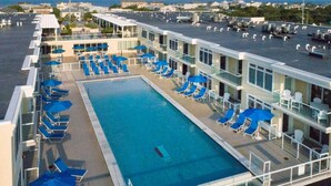 A rooftop pool with blue lounge chairs and umbrellas, surrounded by modern buildings with balconies.