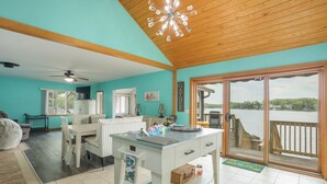 A spacious room with a large table, a white cabinet, and a view of a body of water through a sliding glass door. - Enchanting, Romantic Lakefront Cottage, Close to Frankenmuth (Millington)