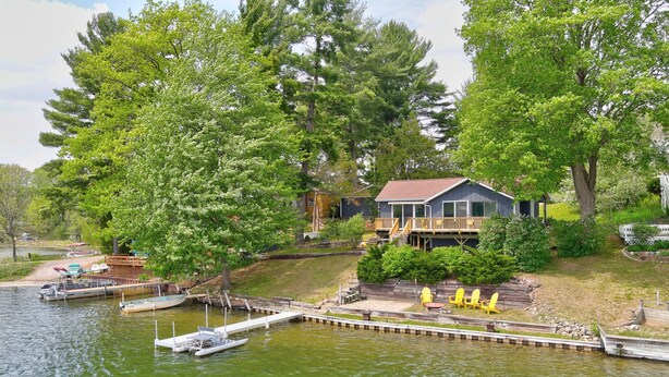 A lakeside property with a dock, boats, and a house with a deck and outdoor seating. - Enchanting, Romantic Lakefront Cottage, Close to Frankenmuth (Millington)