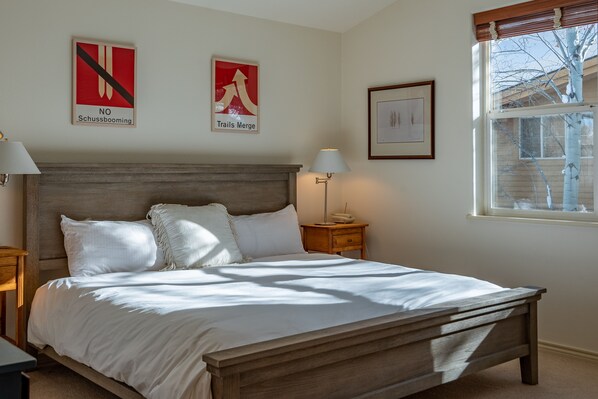 A bedroom with a wooden bed, white bedding, a nightstand with a lamp, and two wall-mounted signs. - Ketchum Condo on Bike Path, Walk to town (Ketchum)