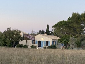 Ein rustikales Haus mit Ziegeldach, umgeben von hohem Gras und Bäumen.
