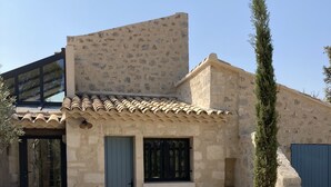 A stone building with a tiled roof, a blue door, and a window with black bars.