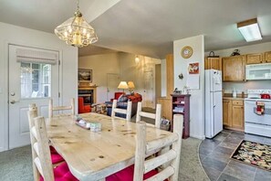 A dining area with a wooden table and chairs, a chandelier, and a kitchen with wooden cabinets and appliances.