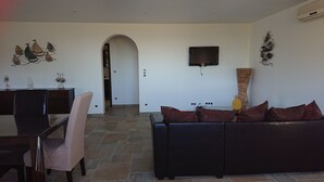 A living room with a sofa, a TV mounted on the wall, and a decorative wall piece. - New detached house (Corbara)