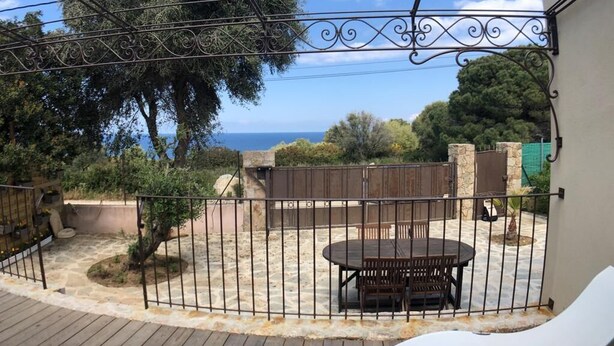 A patio with a round table and chairs, surrounded by a metal fence, overlooking a scenic view with trees and a body of water. - New detached house (Corbara)