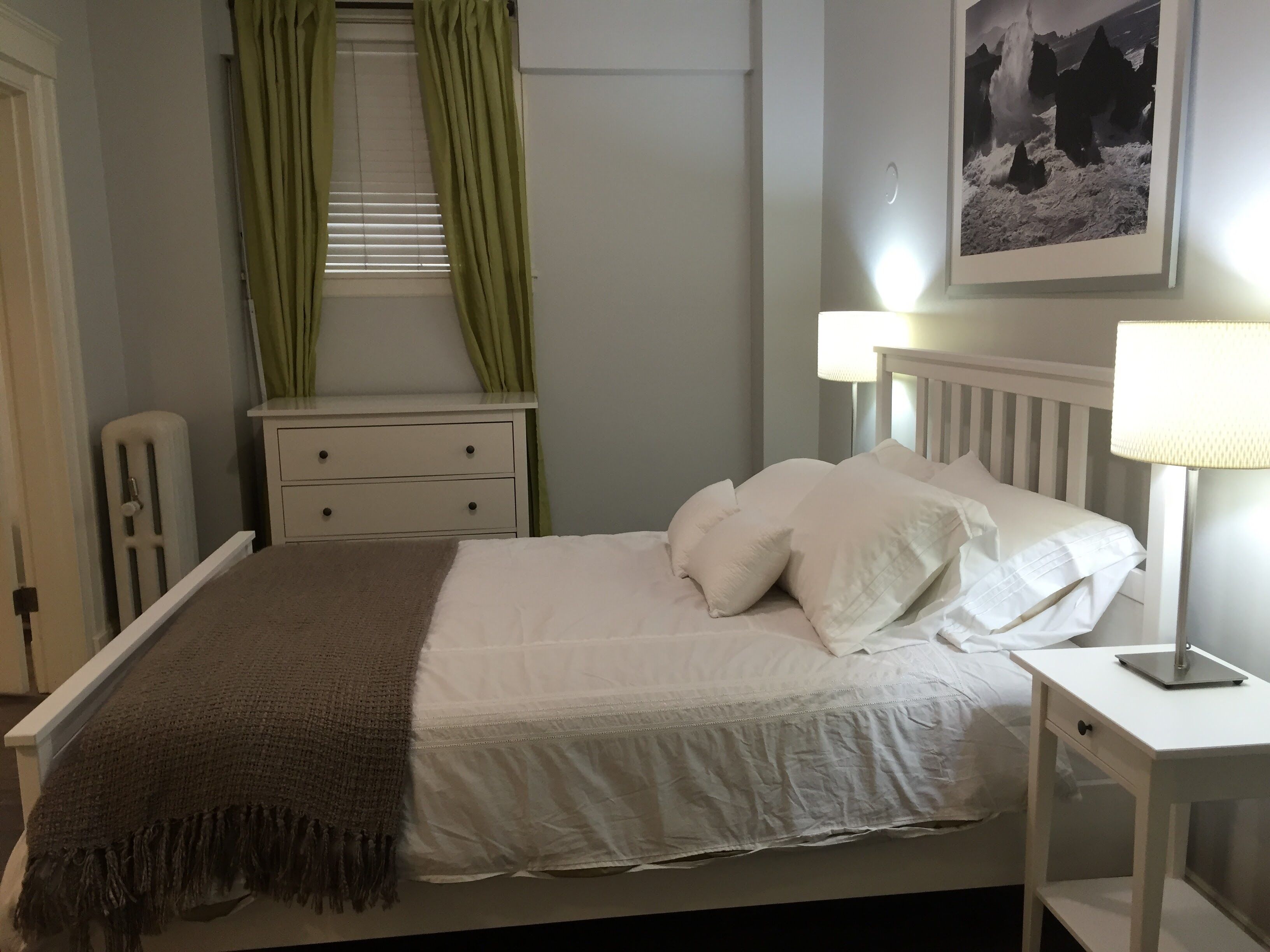 A neatly made bed with white linens and a brown throw blanket, a bedside table with a lamp, and a framed picture on the wall.