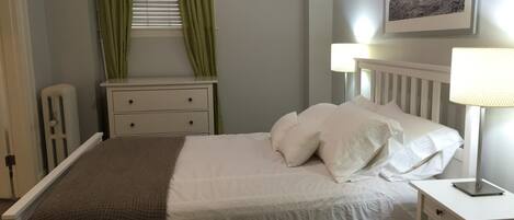 A neatly made bed with white linens and a brown throw blanket, a bedside table with a lamp, and a framed picture on the wall.