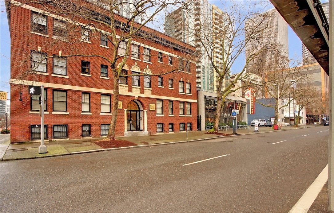 A red brick building with a large arched entrance, a sidewalk, and a street.