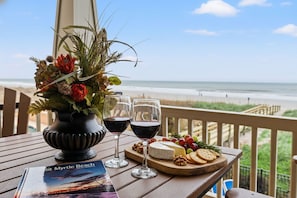 Una mesa con un jarrón de flores, dos copas de vino, una tabla de quesos con galletas y frutos secos, y un folleto titulado 'Visit Myrtle Beach'.