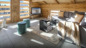 A log cabin interior with a sofa, television, and ottomans. - Chalet Argali - luxury ski-in ski-out base for 14 - OVO Network (Le Grand-Bornand)