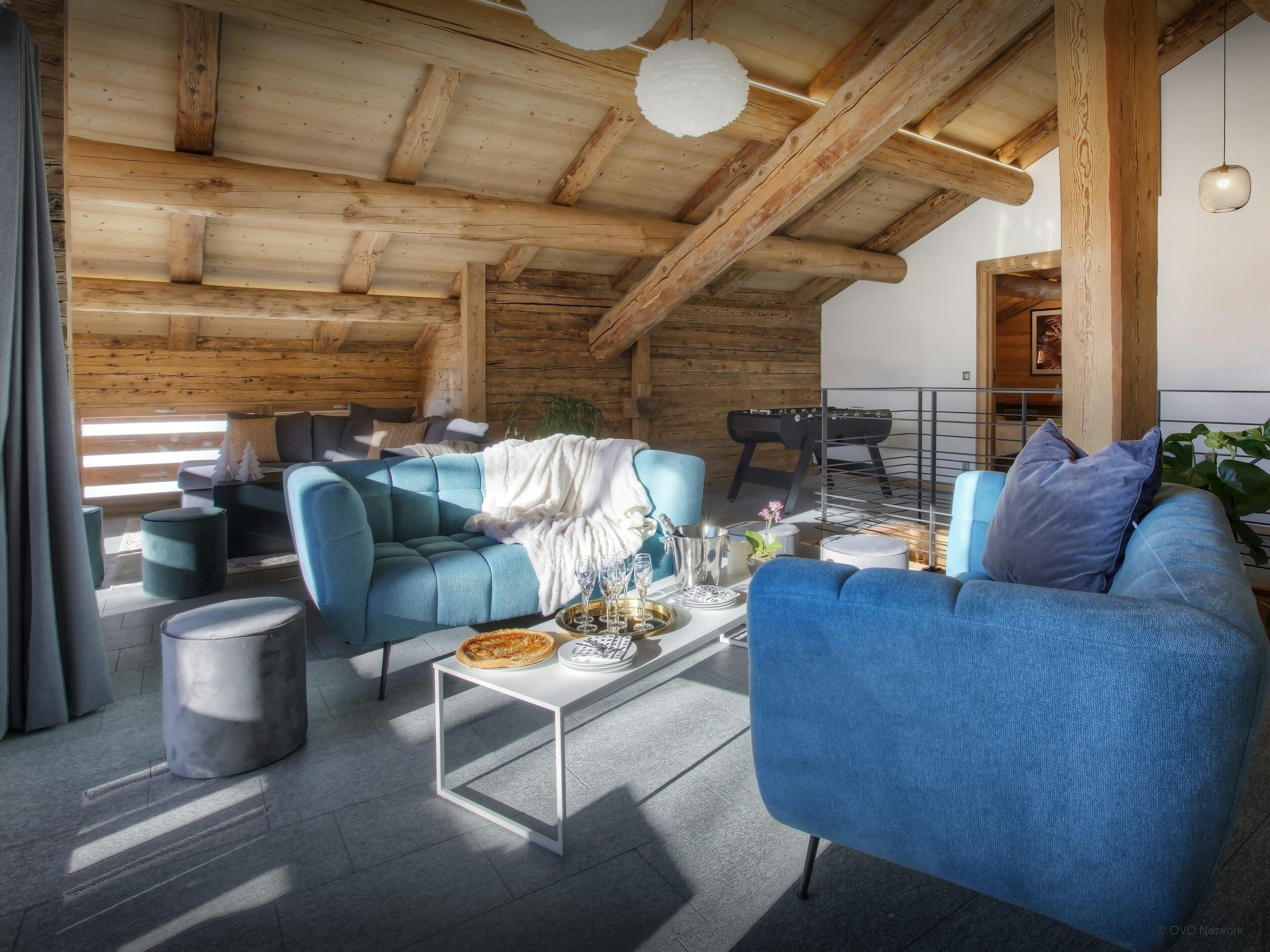 A cozy living room with blue sofas, a coffee table, and a wooden ceiling.