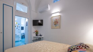Ein Hotelzimmer mit Bett, Fernseher, einem Gemälde und einem Schreibtisch mit Blumenvase.