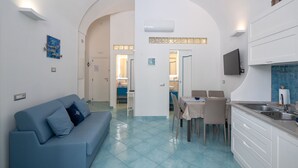 Eine moderne Küche mit weißen Schränken, ein Essbereich mit Tisch und Stühlen sowie ein Wohnzimmer mit Sofa und Fernseher.