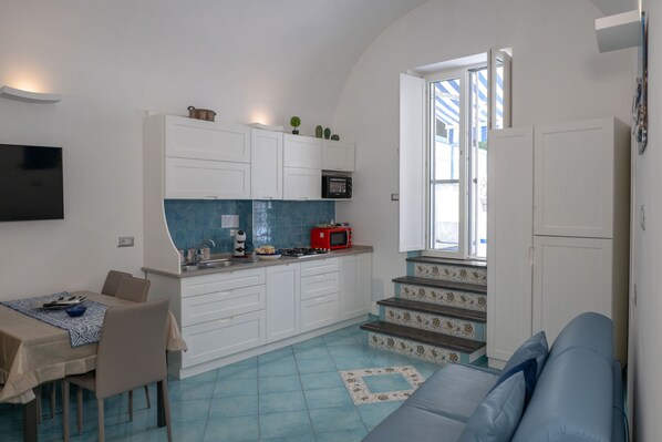 A compact kitchen with white cabinets, a red microwave, and a blue tiled backsplash.