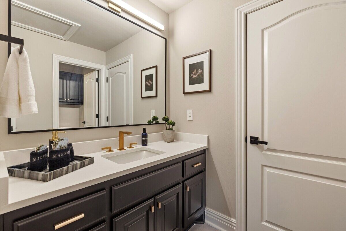 A bathroom with a large mirror, two sinks, dark cabinets, and a towel rack.