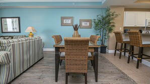 A living room with a sofa, wicker chairs, a dining table, and a kitchen area. - Perfect Location, Perfect View
11th FL - 2 Bd, 2 Ba - Beachfront (Panama City Beach)
