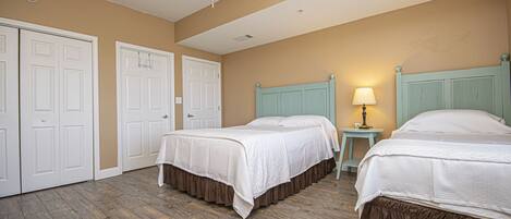 A hotel room with two beds, a ceiling fan, a nightstand with a lamp, and a door.