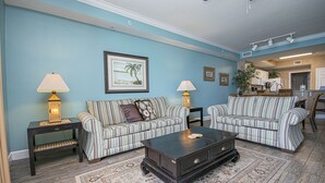 A living room with two striped sofas, a dark coffee table, and two lamps. There is a framed picture on the wall and a kitchen area in the background. - Perfect Location, Perfect View
11th FL - 2 Bd, 2 Ba - Beachfront (Panama City Beach)