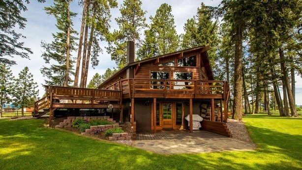 Une cabane en rondins à deux étages, dotée d’une terrasse et entourée de grands pins.