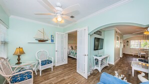 A spacious living room with a blue sofa, wicker chairs, a ceiling fan, and a wooden floor.
