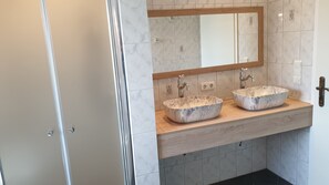 Une salle de bain avec deux vasques en marbre, un meuble-lavabo en bois et un grand miroir.