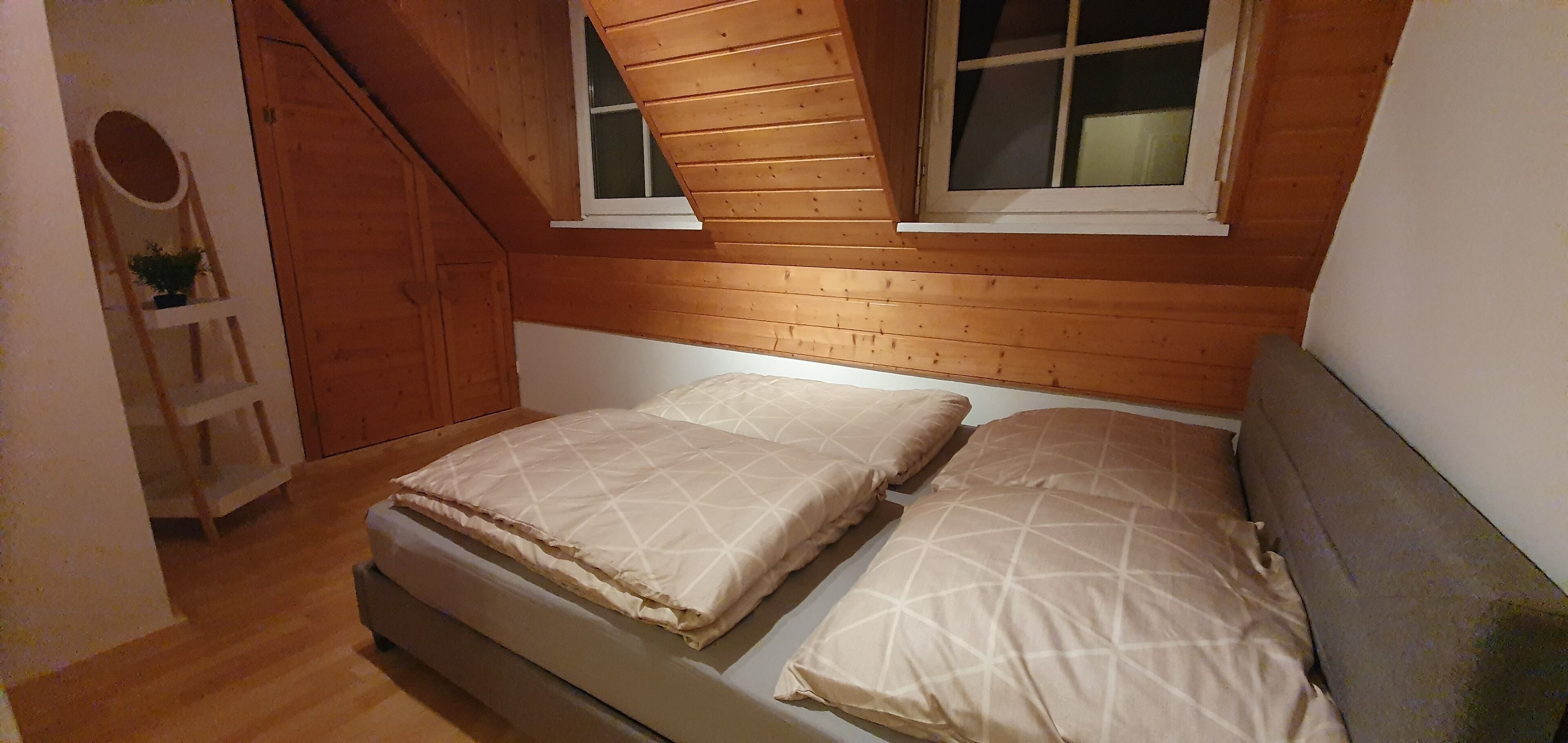 A small, cozy room with a sloped ceiling, wooden walls, and a bed with two pillows.