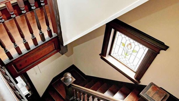 Una escalera de madera con barandilla de metal, un ventanal con diseño de vitral y un tapete texturizado al pie.