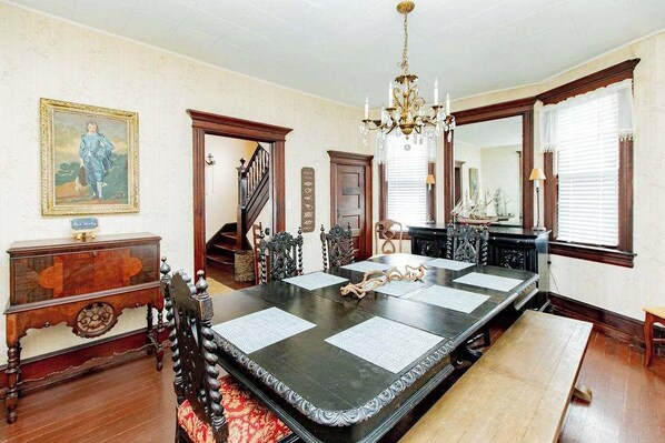 A formal dining room with a long table, chairs, a chandelier, and a staircase.