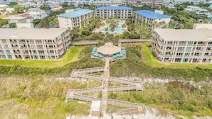 Un resort con piscina central, varios balcones y un paseo marítimo que lleva a la playa.