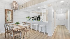Una cocina moderna con armarios blancos, una isla central y un comedor con sillas y una mesa de madera.