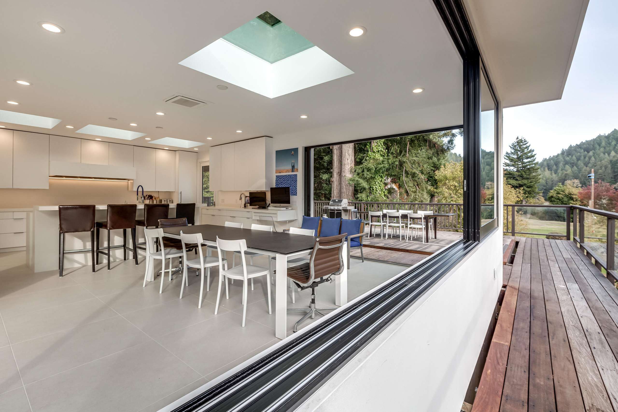 A modern kitchen with a dining area and a deck overlooking a forested area.