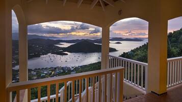 Un balcon fermé offrant une vue sur une baie où se trouvent des bateaux, ainsi que sur un paysage montagneux.