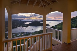Un balcon fermé offrant une vue sur une baie où se trouvent des bateaux, ainsi que sur un paysage montagneux.
