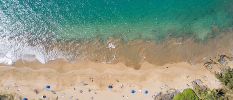 Ein Strand mit klarem türkisblauem Wasser, sandigem Ufer und sonnenbadenden Personen.