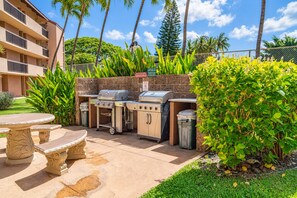 An outdoor patio with a grill, trash bins, and a table.