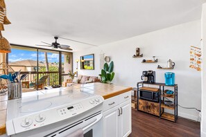 Una cocina moderna con un amplio ventanal, un ventilador de techo y una zona de comedor con sofá y mesa.