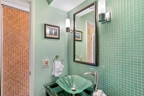 A bathroom with a glass sink, a mirror, and green tiled walls.
