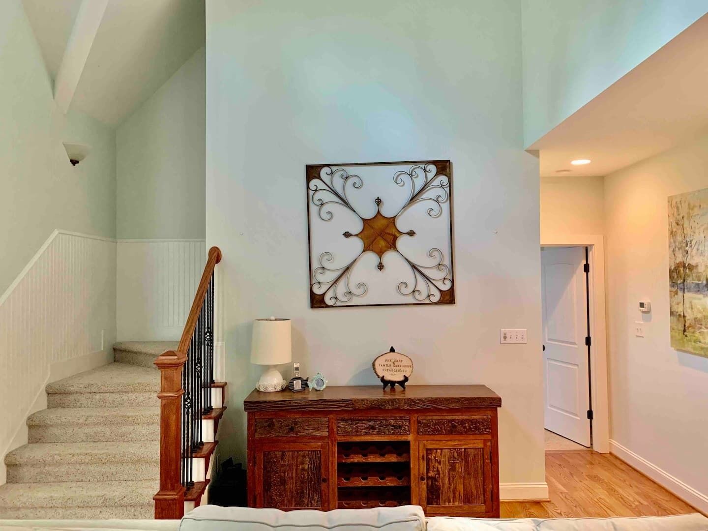 A staircase with a wooden handrail leading to a landing. A decorative metal piece is mounted on the wall above a wooden console table with a lamp and a clock.