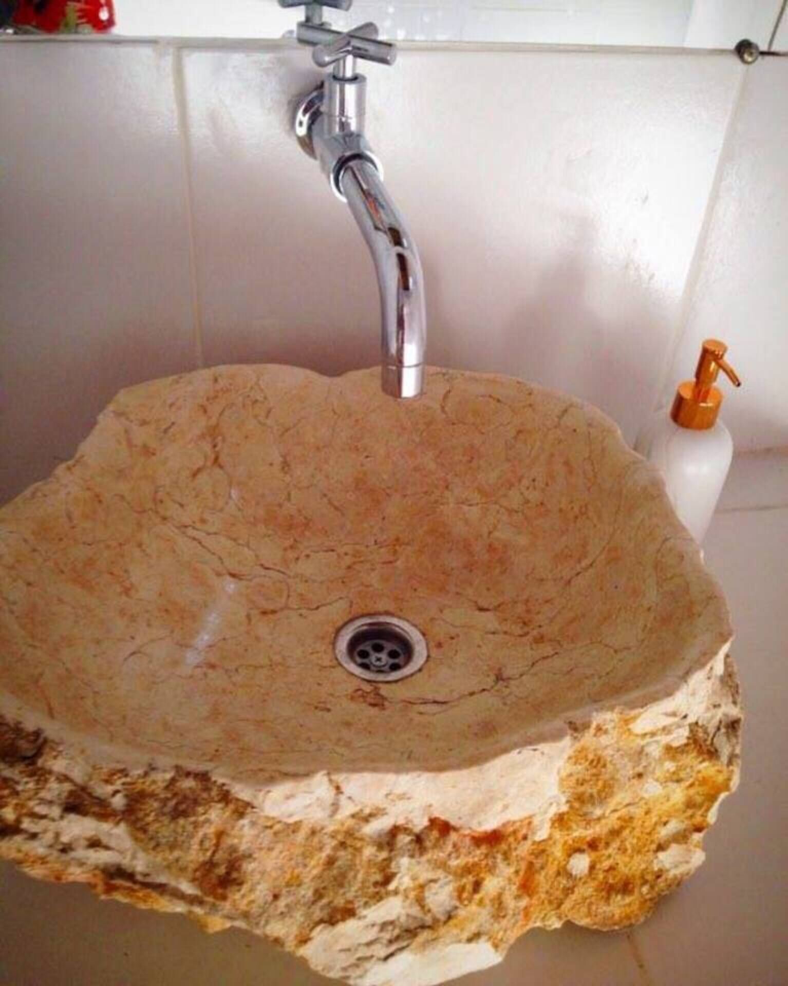 Un baño con un lavabo de piedra, un grifo y dispensador de jabón.