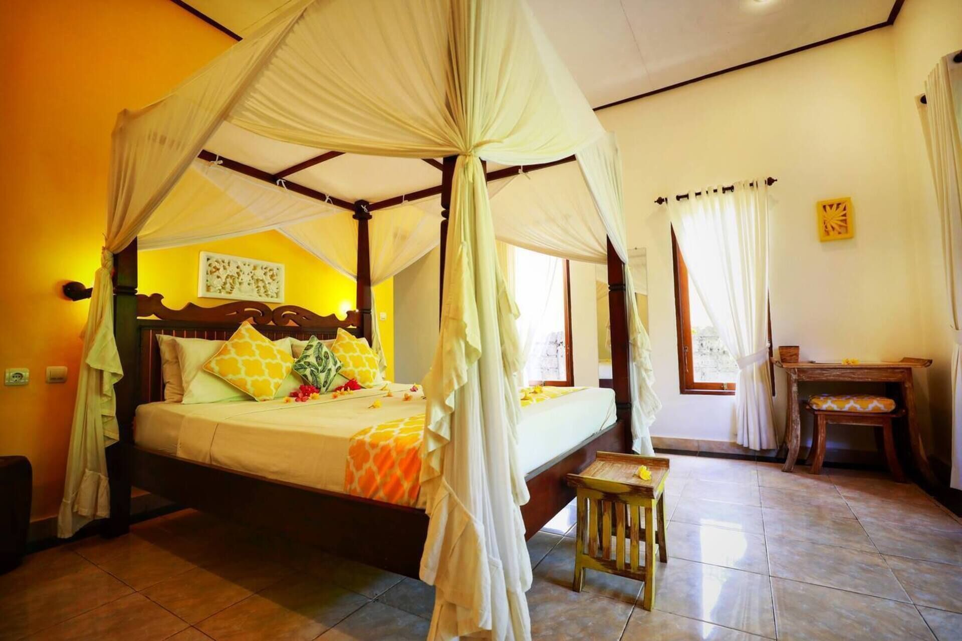 A four-poster canopy bed with a wooden headboard, a bedside table, and a small stool.