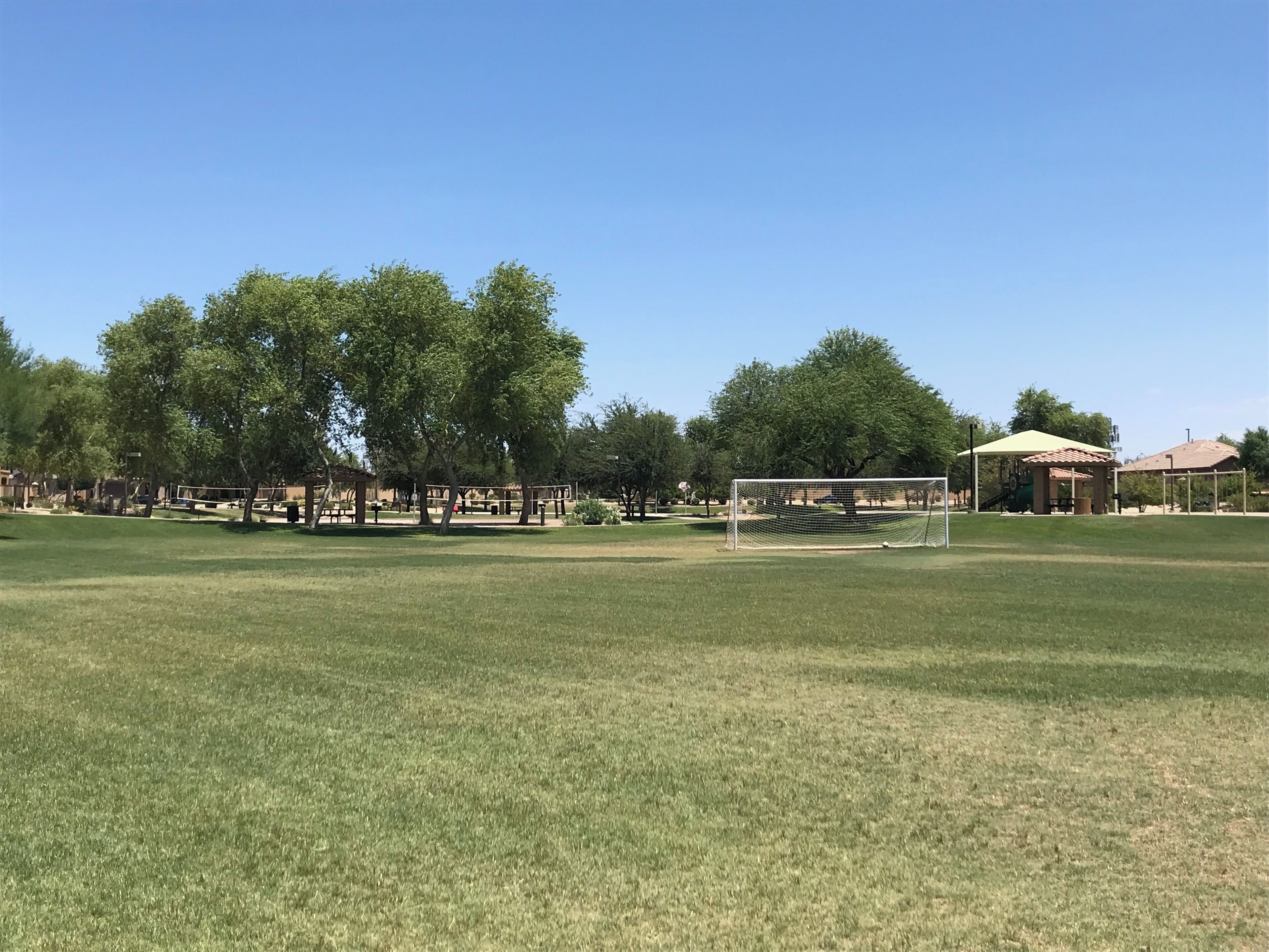 Un terrain herbeux avec des buts de football, des arbres et un pavillon.